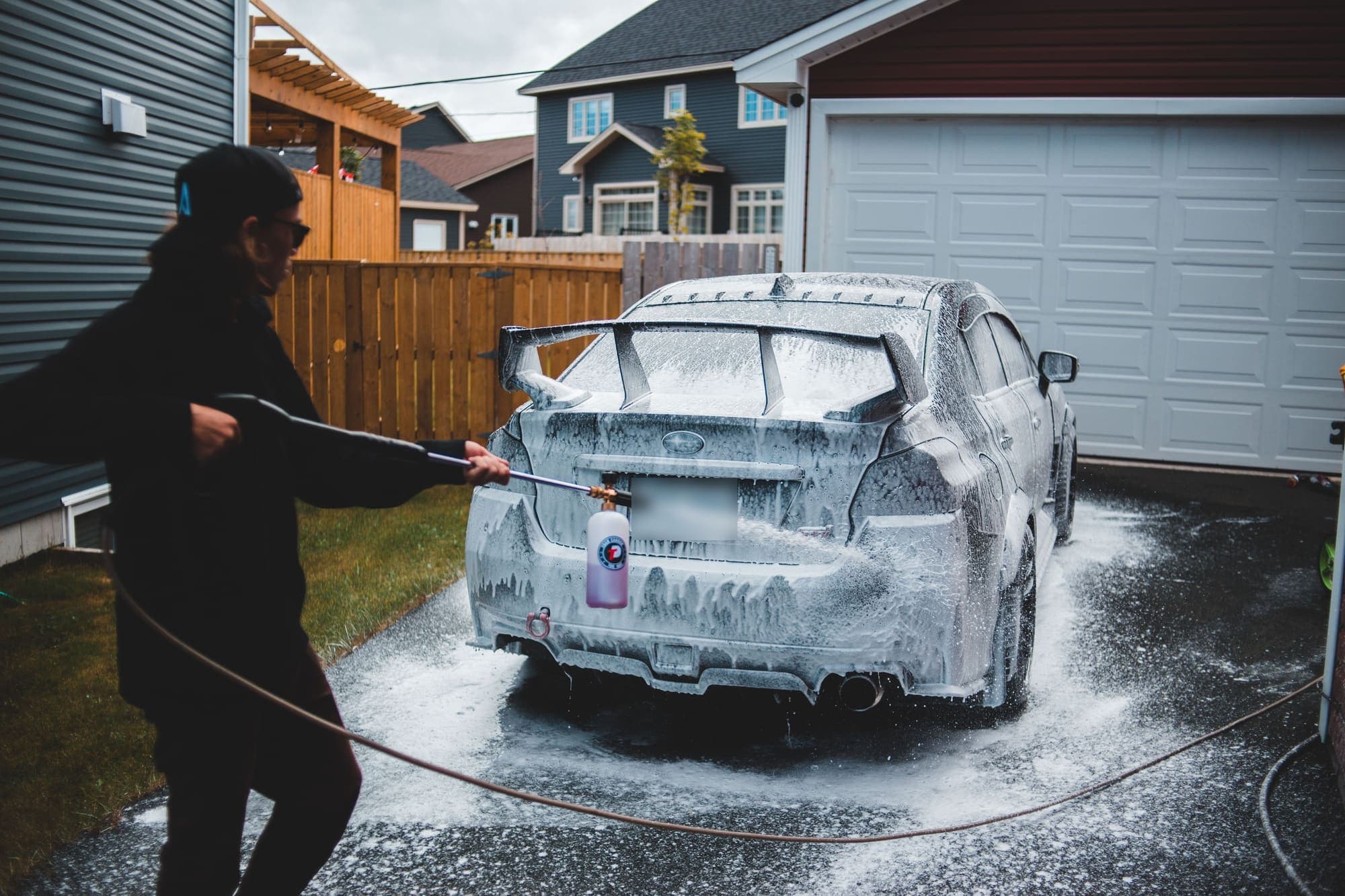 A detailer foaming a car in a suburban driveway