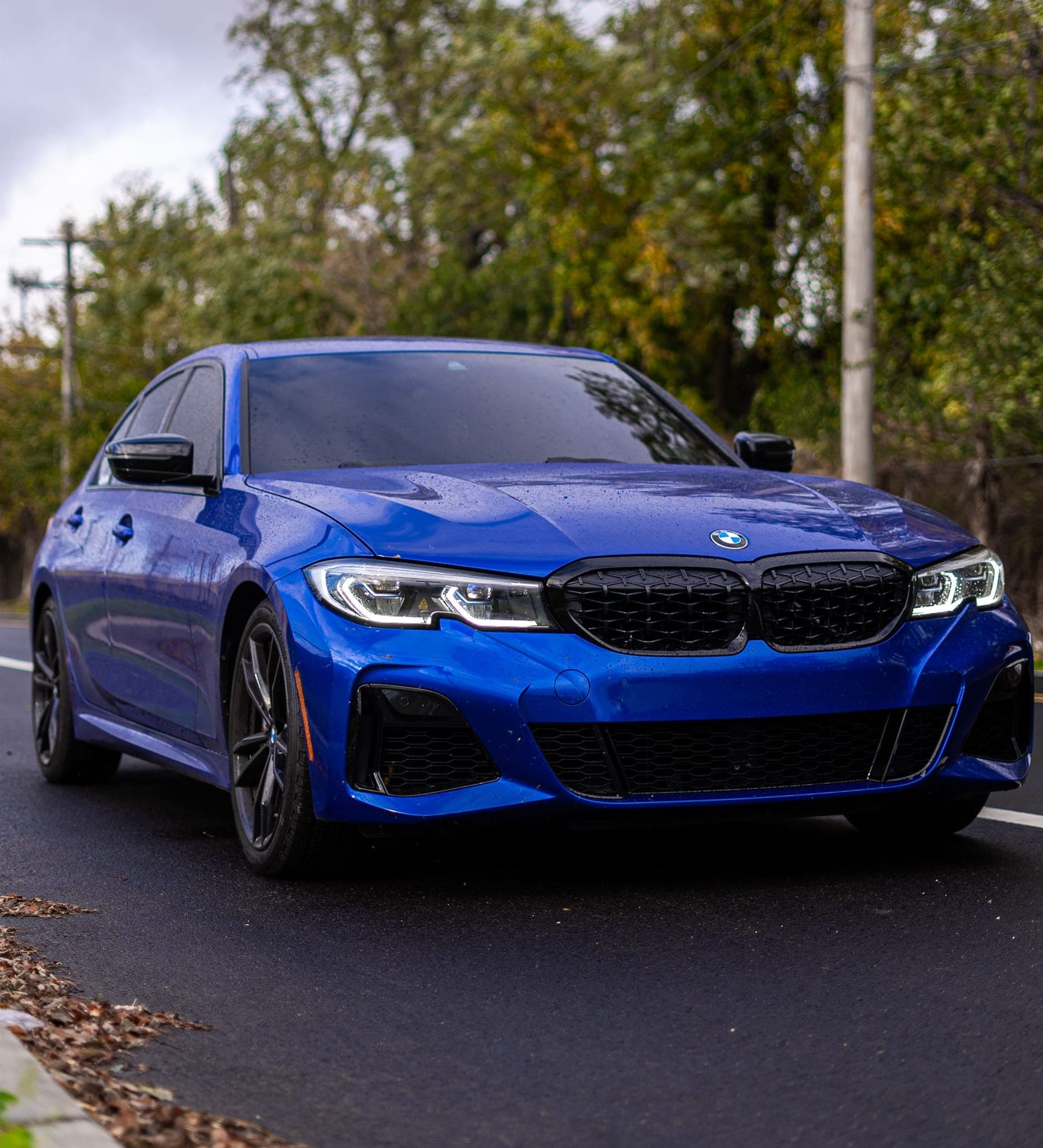 A Portimao Blue BMW M340i, freshly washed, beaded with water on a wet autumn road